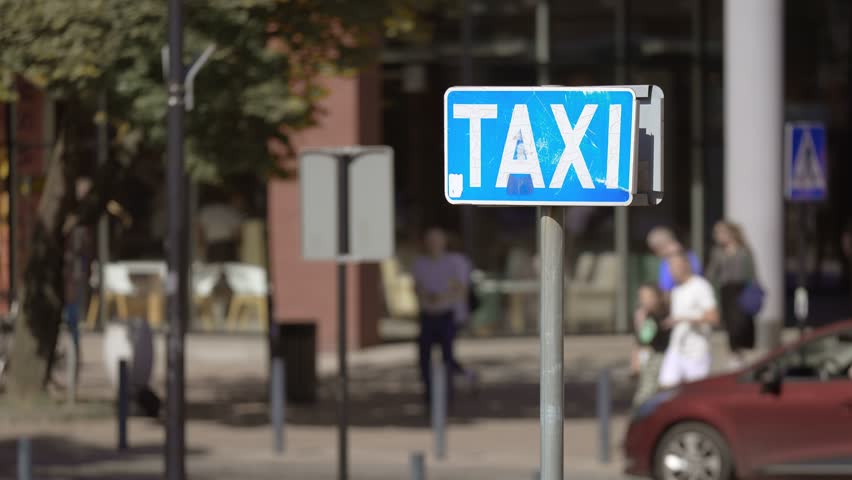 Busy Street Corner With Taxi Sign in Focus Outside Commercial Buildings on Sunny Day at Polish city Gdansk. Taxi station sign on blurred town street with lot of people and automobiles