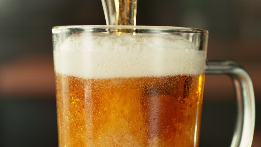 Super Slow Motion of Pouring Beer into Pint in Detail. Filmed on High Speed Cinema Camera, 1000 fps. Blur Industrial Interior on Background. Camera in Motion.