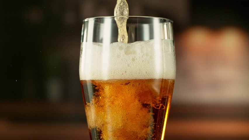 Super Slow Motion of Pouring Beer into Pint in Detail. Filmed on High Speed Cinema Camera, 1000 fps. Blur Industrial Interior on Background.