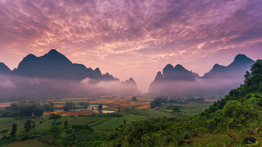 Timelapse of dramatic landscape of vibrant sunrise over mountain range with foggy, river and local village in Phong Nam Valley at Cao Bang, Vietnam