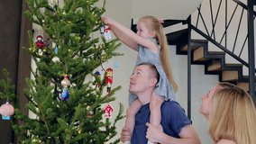 Young family is decorating a christmas tree. The father is holding his daughter on his shoulders while she hangs an ornament on the tree - Powered by Shutterstock - Get 15% off with code: PIKWIZARD15