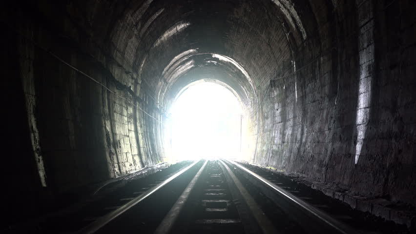 A man is walking in a railway tunnel towards the tunnel exit light.