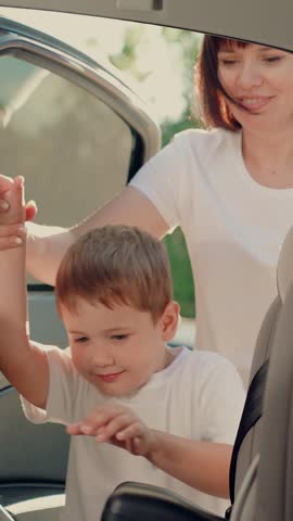 Mother fastens her child son in car seat with seat belt. Mom gets her kid son out of car seat, safe car. Happy family. Family trip. Mom cares about her sons safety. Boy kid sitting in car child seat