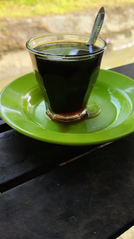 a cup of hot coffee in a small green saucer on a wooden bench