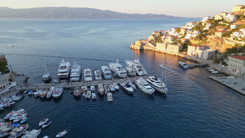 Marvel at the enchanting island of Hydra, where whitewashed buildings hug the rocky shoreline, surrounded by crystal-clear waters and picturesque scenery at twilight.