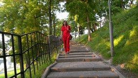 An elderly woman in red clothes walks in the park. She walks down a staircase surrounded by green trees. - Powered by Shutterstock - Get 15% off with code: PIKWIZARD15