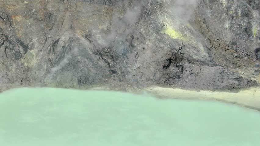 Aerial view of Kawah Putih, Bandung, features its captivating turquoise lake, bordered by stark white volcanic terrain. The ethereal mist creates a tranquil atmosphere in this stunning natural wonder.