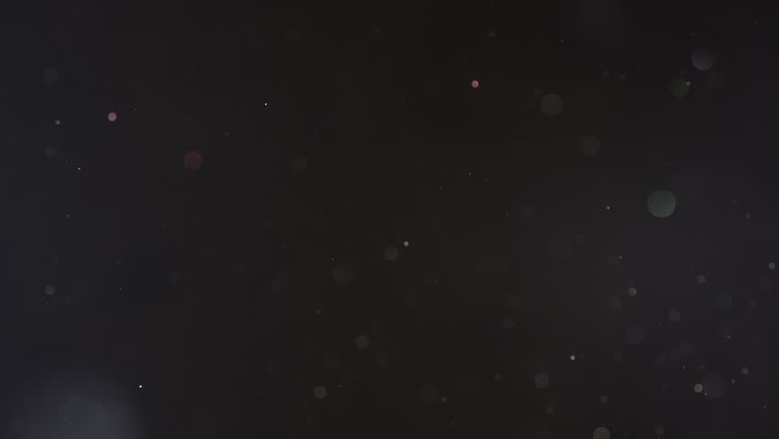 Beautiful shiny dust particles fly abstract black bokeh background. Glitter floating air. Magic glow sequins close up. Iridescent sparkles shimmer. Blurry spangles waving. Holiday Christmas decoration