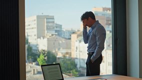 Exhausted businessman standing at office window. Tired man manager feeling stress worried work problem at modern workplace. Fatigued employee looking city view experiencing business crisis indoors. - Powered by Shutterstock - Get 15% off with code: PIKWIZARD15