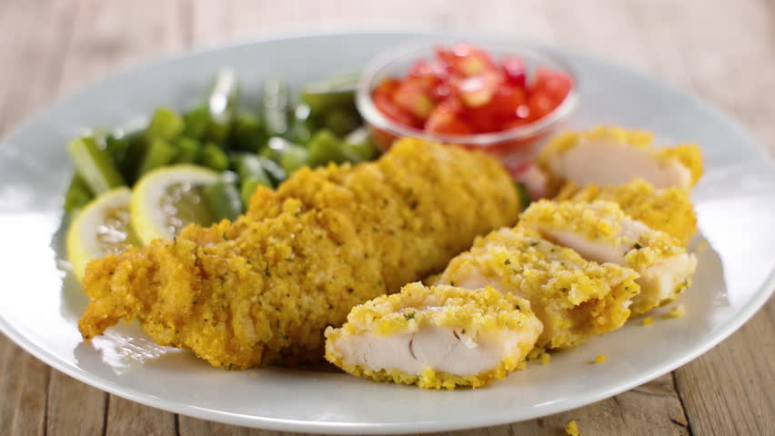 Plate of crispy fried chicken with vegetable salad and a fork. Ideal for comfort food and balanced meals
