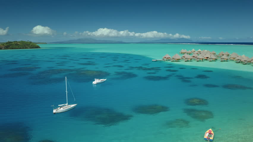 Two sailboats yachts anchor near shallow turquoise water lagoon near tropical island, luxury resort overwater bungalows in background. Maldives remote wild nature paradise, exotic summer luxury travel