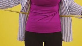 Young woman in casual wear carefully measuring waist size with tape, showcasing health trends. Fitness, fashion, diet, lifestyle concept. Yellow background - Powered by Shutterstock - Get 15% off with code: PIKWIZARD15