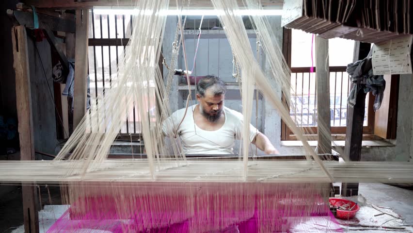 Indian mature man sitting at handloom weaving with purple thread