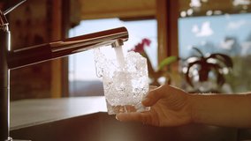 SLOW MOTION, LENS FLARE, CLOSE UP: Hand holds a glass under a kitchen faucet, with water splashing and filling glass in bright morning sunlight. Simplicity of pouring fresh glass of drinking tap water - Powered by Shutterstock - Get 15% off with code: PIKWIZARD15