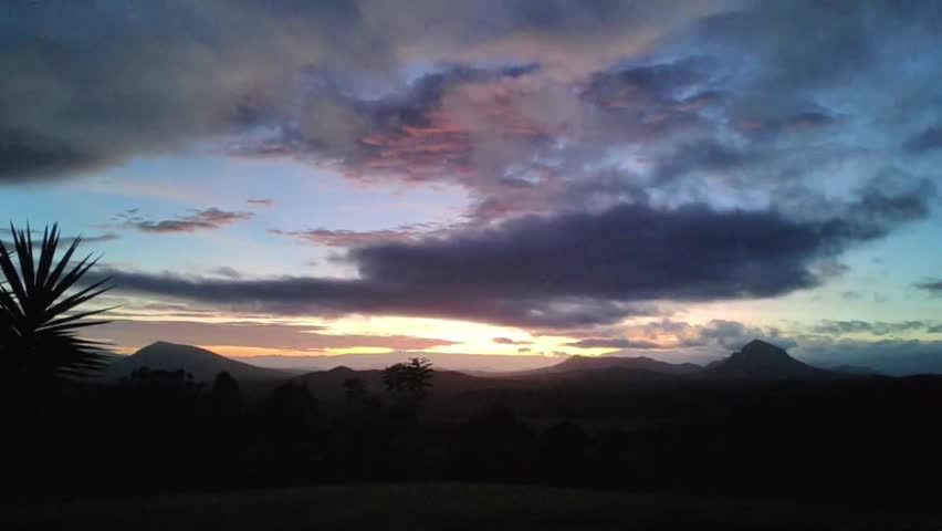 A landscape timelapse scene of cloudy sky moving over lake with trees at sunset.  green mountains covered with moving the sun brightness, morning sunrise from dawn to day light.