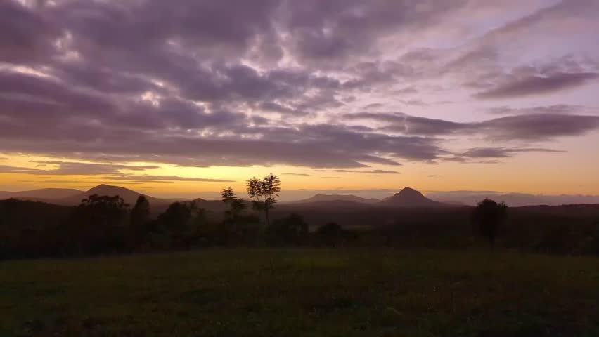 A landscape timelapse scene of cloudy sky moving over lake with trees at sunset.  green mountains covered with moving the sun brightness, morning sunrise from dawn to day light.