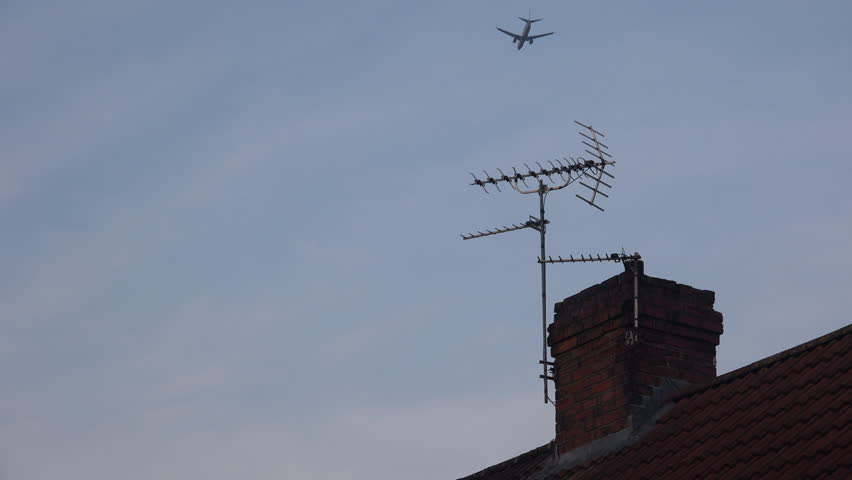 Chimney and house roof with television antenna aerial and low flying passenger jet going overhead England UK 4K