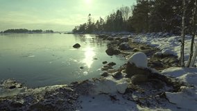 A serene winter scene unfolds by a partially frozen lake, showcasing shimmering reflections under the early morning sun and soft snow covering the shore.	 - Powered by Shutterstock - Get 15% off with code: PIKWIZARD15