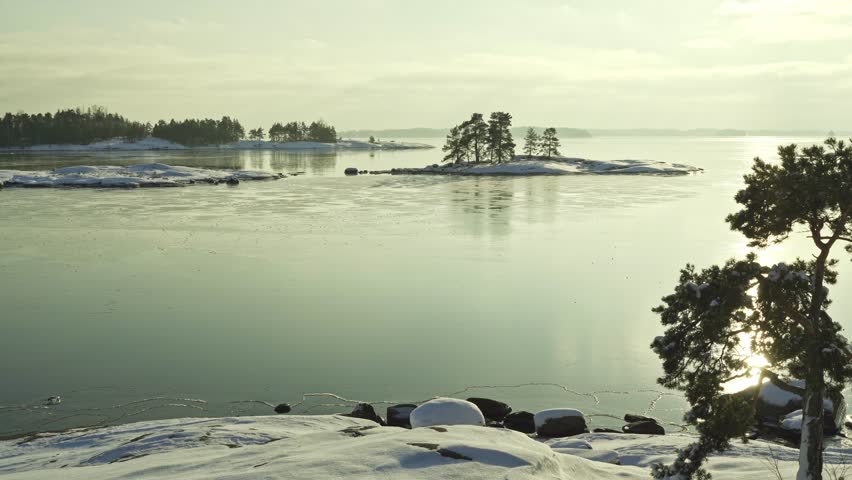 Explore the tranquil beauty of a winter morning where a frozen lake reflects soft sunlight. Distant islands and snowy terrain create a peaceful escape in nature.	
