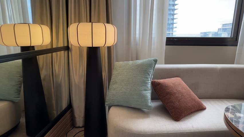 Warm cosy hotel room at Pan Pacific Perth. Stylish pedestal lamp, sofa and cushions near window.