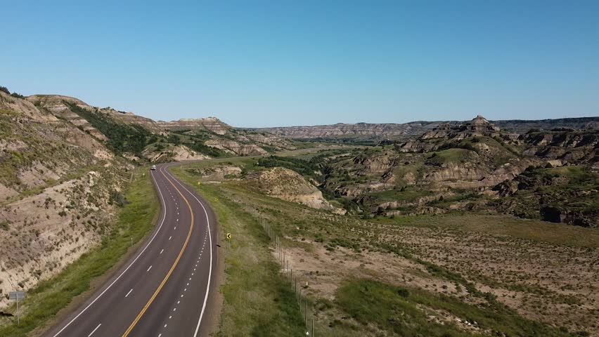 Aerial shot of truck climbing a hill in the badlands. The road is on the left with the landscape stretching into the distance.