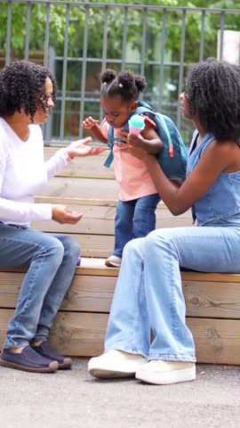 Mother and grandmother showing a game to a girl outdoors when they picking up from school