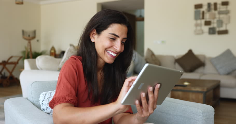 Smiling Latina woman using digital tablet for on-line shopping, remote communication with friend, making order, contact to client, teleworking from home. Modern tech, internet and e-dating app usage