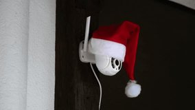 White CCTV camera in red Santa Claus hat rotates and records moving objects. Outdoor video surveillance. Security system. Web cam. Web street control. Distance watch. Smart tech. Footage. Copy space - Powered by Shutterstock - Get 15% off with code: PIKWIZARD15