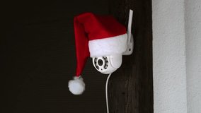 White CCTV camera in red Santa Claus hat rotates and records moving objects. Outdoor video surveillance. Security system. Web cam. Web street control. Distance watch. Smart tech. Footage. Copy space. - Powered by Shutterstock - Get 15% off with code: PIKWIZARD15