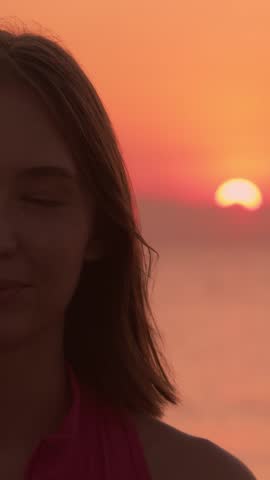 A woman smiles peacefully at sunrise on the beach, her face reflecting calmness after a meditation session. Ideal for content focused on mindfulness, relaxation, and outdoor wellness. Vertical video.
