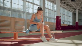 Young woman athlete touches knee feeling pain sitting on bench in sports club. Lady in sportswear carefully massages leg to reduce tension in muscles - Powered by Shutterstock - Get 15% off with code: PIKWIZARD15