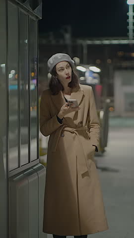 A woman wearing a stylish winter coat is talking on her smartphone during the night