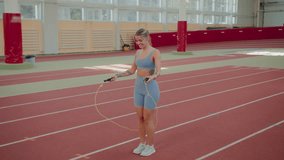 Smiling young woman engages in jumping rope at indoor stadium. Sportive blonde female improves physical health performing active exercise during workout - Powered by Shutterstock - Get 15% off with code: PIKWIZARD15
