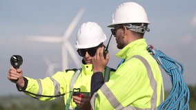 Two engineers wearing high visibility safety jackets and helmets measure wind speed with an anemometer and analyze data on a tablet at a renewable energy site. The cloudy sky adds depth to the scene. - Powered by Shutterstock - Get 15% off with code: PIKWIZARD15