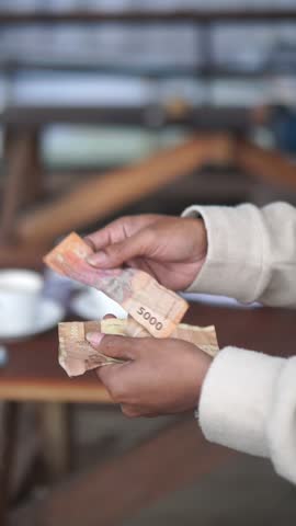 A man is counting five thousand rupiah notes with his hands.