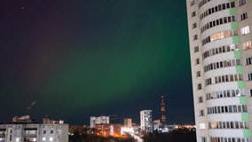 Aurora borealis lighting up the night sky with vibrant green hues, captured in timelapse above a cityscape featuring residential buildings and a communication tower - Powered by Shutterstock - Get 15% off with code: PIKWIZARD15
