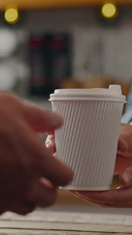 A pair of hands reaches out to pass a disposable coffee cup at a cafe, with warm lighting creating an inviting atmosphere, perfect for starting the day