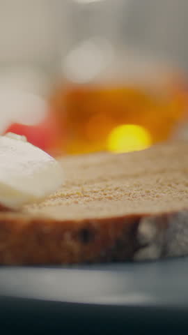 A hand is adding salt to a sandwich. The sandwich is on a wooden cutting board. There are slices of tomato and cheese on top of a slice of bread