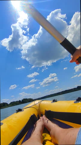 Woman floating in inflatable yellow boat and paddling on river or lake with shining sun on blue sky with white clouds on hot summer day. Person floating in kayak. POV. Sports tourism recreation motion
