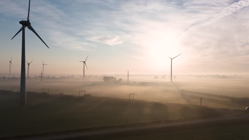 Wind turbines generating electricity in morning fog while a train passes by