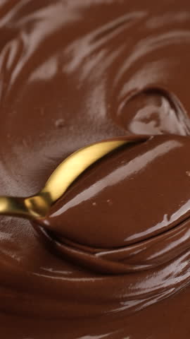 Stirring melted chocolate with golden spoon, close up. Liquid chocolate swirl