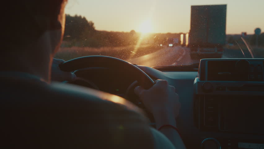 Young man steers the car in heavy traffic on the highway full of trucks