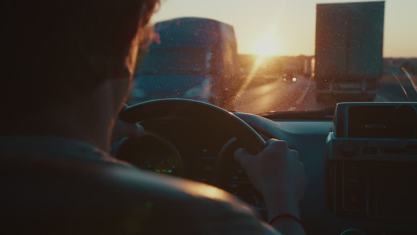 Young man steers the car in heavy traffic on the highway full of trucks