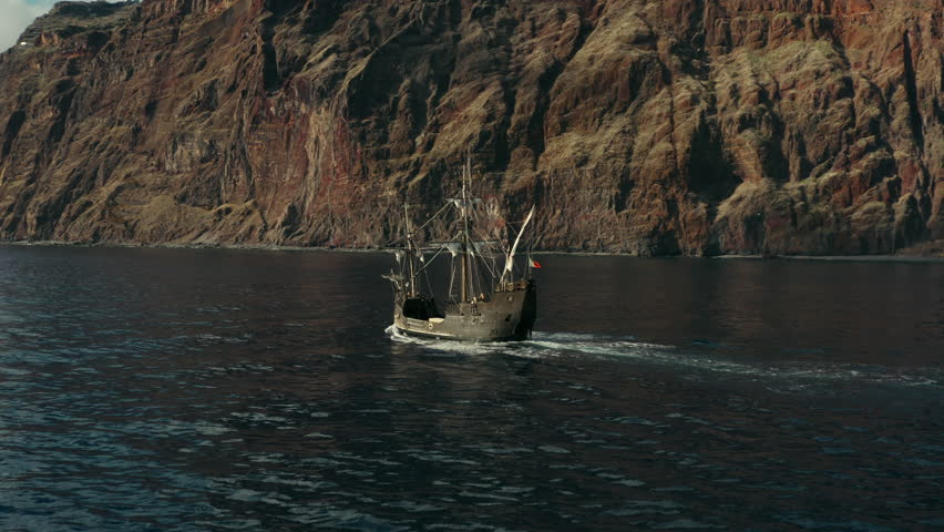 Scenic aerial view of Christopher Columbus ship replica Santa Maria sailing with a dramatic sea cliff in the background in Madeira