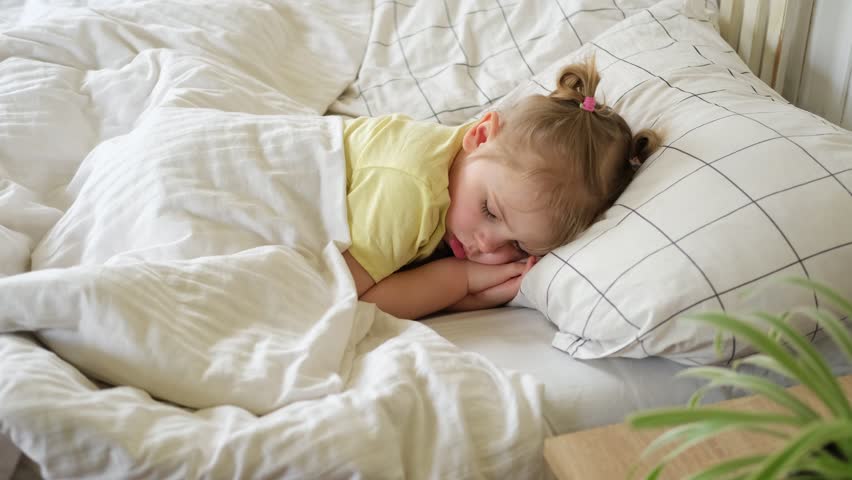 Peaceful adorable baby sleeping on a bed at home. Slumbering little child. Two years old girl sleeps peaceful at domestic room interior background. Serene dream. Cute face close up. Deep kid slumber