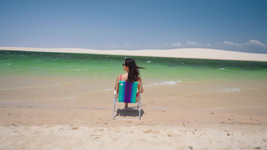 Woman sits and relax on desert dunes between rain water lagoons. Brazil Northeast.
