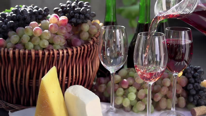 Pouring a Glass of Rose Wine. In pouring a glass of wine on the background of a basket with grapes, wine bottles and pieces of cheese. Slow Motion