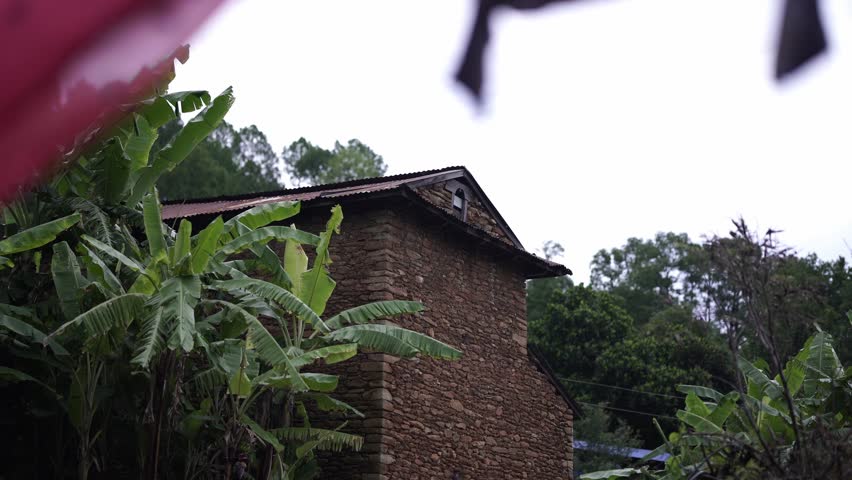 Drying clothes in front of a traditional house in a Nepali village, with greenery surrounding the background