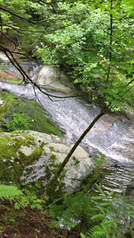 A calming smooth waterfall sends a stream of water through the forest surrounded by greenery in the Adirondack Mountains. 