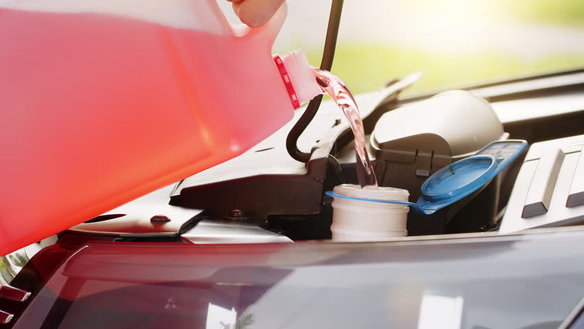 Service worker man pours into car hood engine room windscreen red cleaning washer liquid automobile glass cleaner from canister bottle. Windshield fluid water into windshield washer tank reservoir